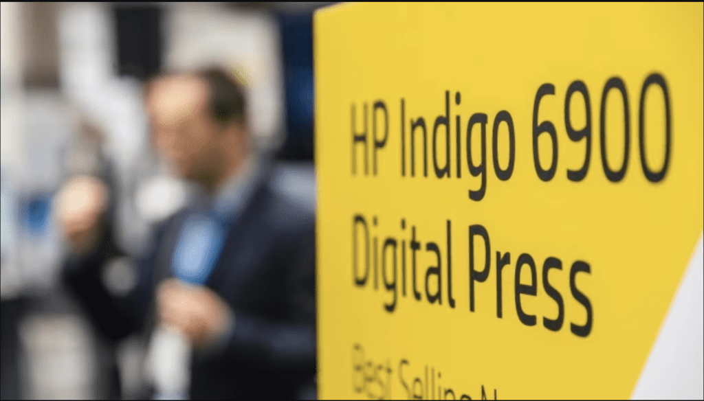 Gelbes Plakat mit der Aufschrift "HP Indigo 6900 Digital Press Best Selling" als Sinnbild für contact investiert in HP Indigo Digitaldruckmaschine