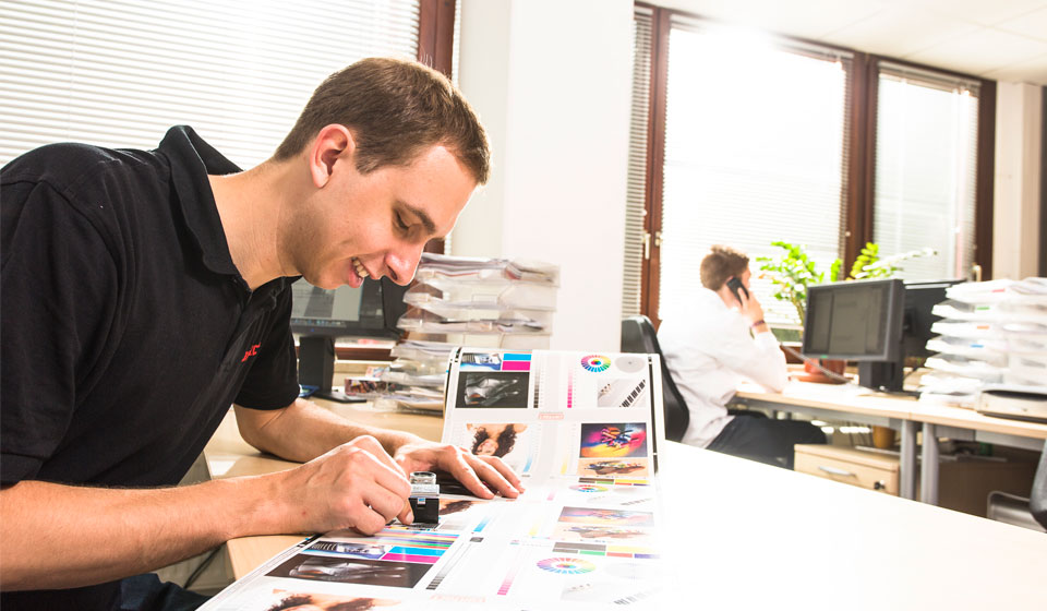 Bild im Büro mit Mann, der Druckergebnisse  kontrolliert als Sinnbild für die leistungsfähige Druckvorstufe von contact.